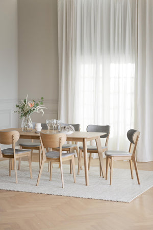 Runt matbord i ljust trä med sex stolar med grå klädsel i modern skandinavisk matsal