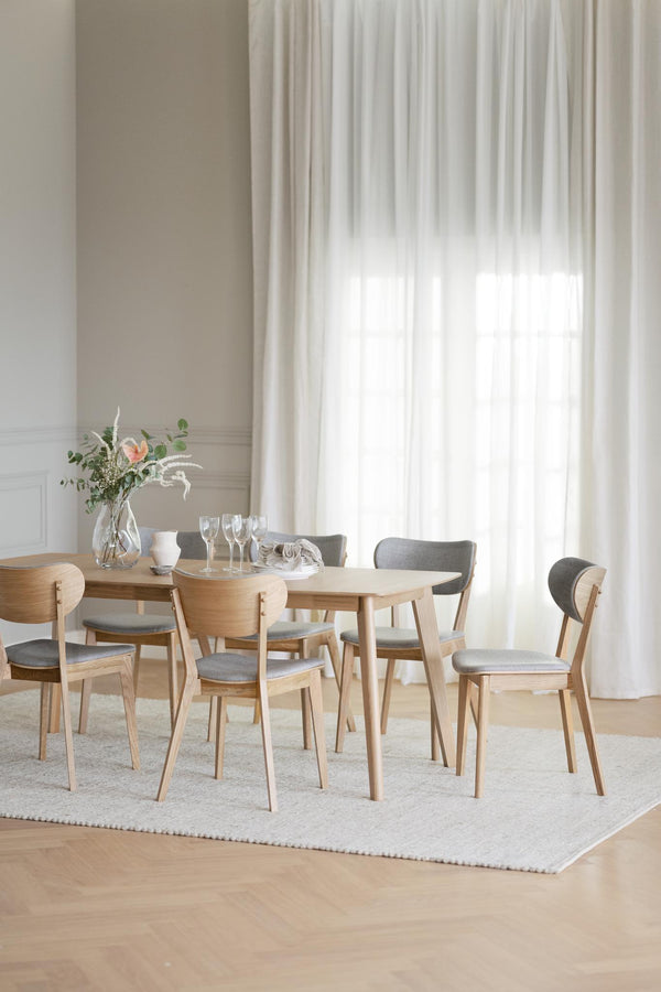 Runt matbord i ljust trä med sex stolar med grå klädsel i modern skandinavisk matsal