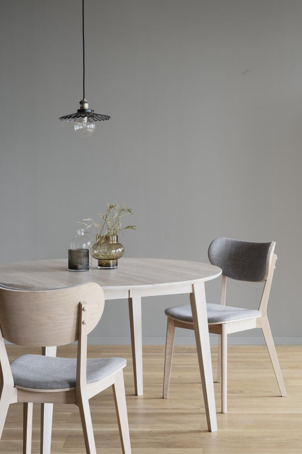 Rund matbord i ljust trä med stolar i grå tyg och pendant-lampa ovanför i modern skandinavisk matsal