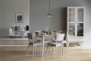 Matgrupp i ljust trä med stolar och bänk i skandinavisk stil, vitrinskåp och soffa i bakgrunden