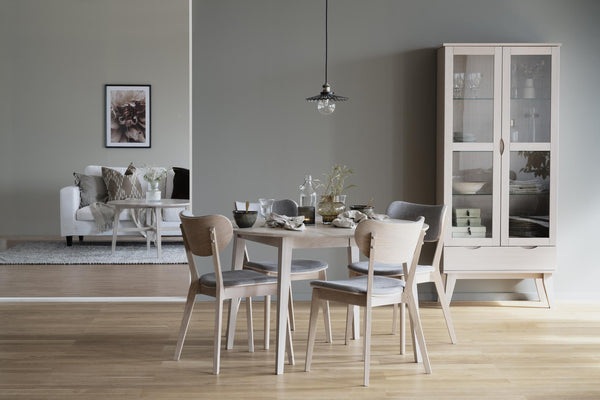 Matgrupp i ljust trä med stolar och bänk i skandinavisk stil, vitrinskåp och soffa i bakgrunden