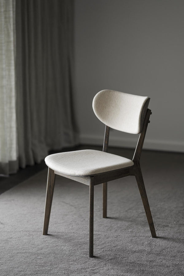 Stol med vit klädsel och mörkt trä på grått golv i minimalistisk inredning