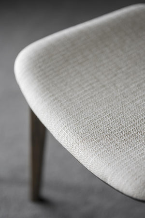 Närbild på vit stol med klädsel i ljust tyg och träben, detalj av sits och rygg