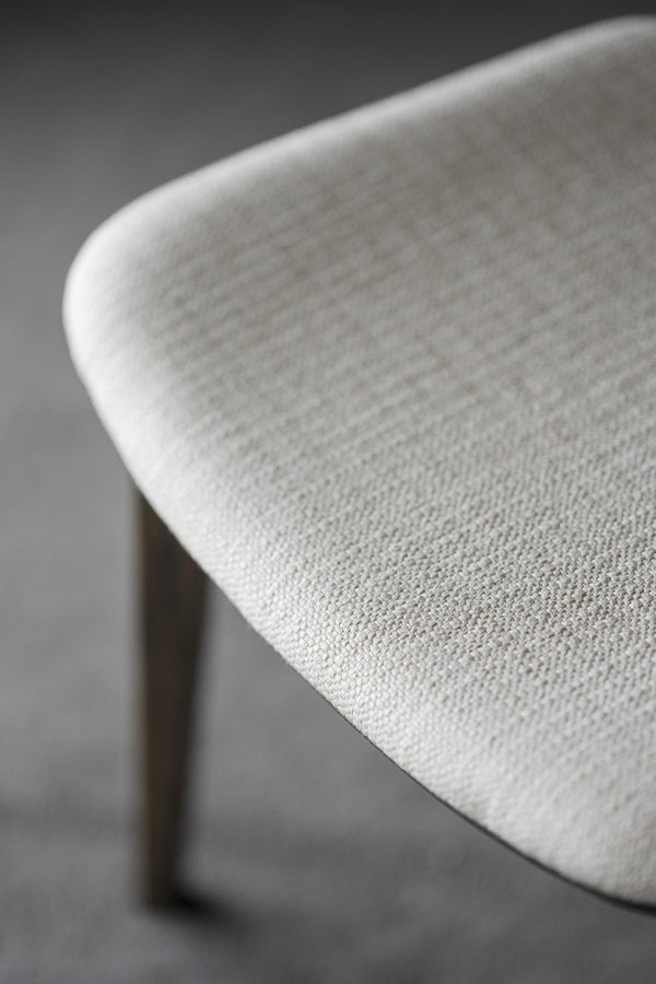 Närbild på vit stol med klädsel i ljust tyg och träben, detalj av sits och rygg