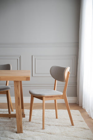 Matstol i ek med grå klädsel vid matbord i ljust matrum med vit väggpanel