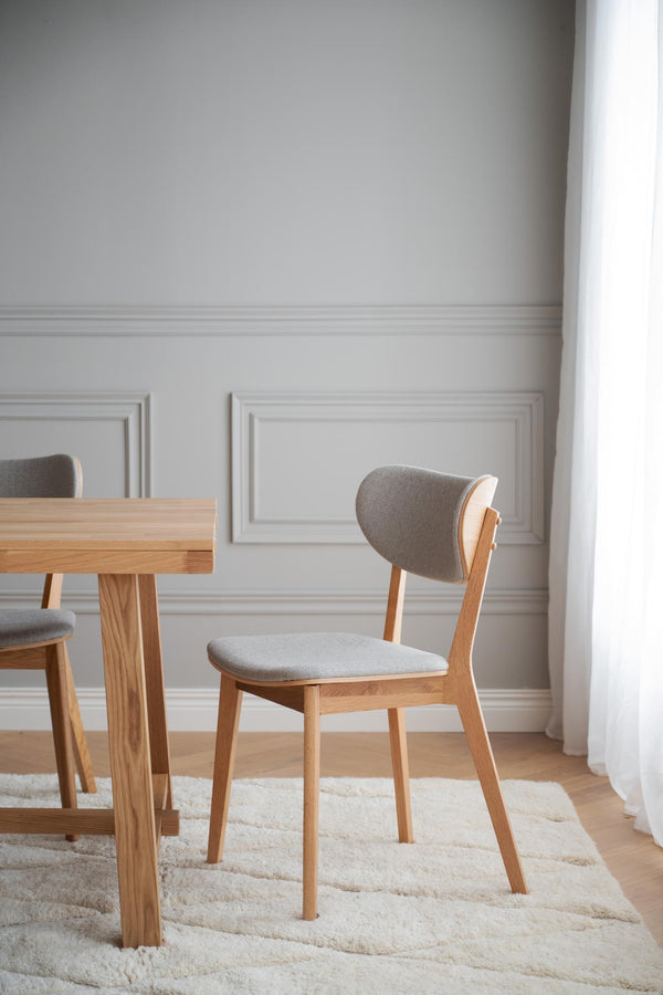 Matstol i ek med grå klädsel vid matbord i ljust matrum med vit väggpanel