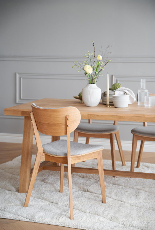 Matbord i ek med matchande stolar med grå dynor i skandinavisk matsal med ljusgrå vägg