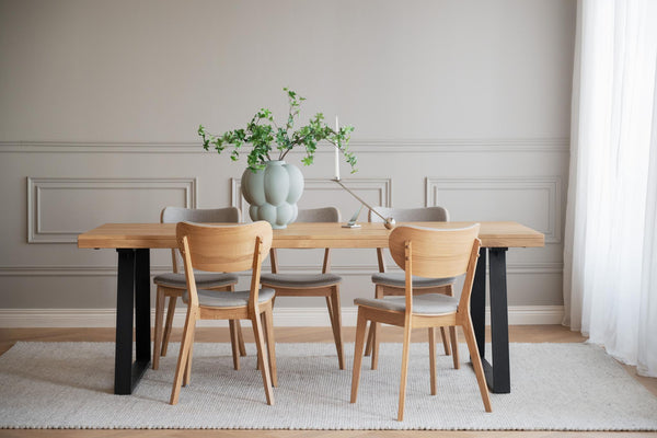 Matbord i ek med svarta ben omgivet av stolar i ljust trä, grön vas med växt som dekoration
