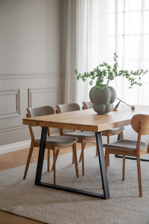 Matgrupp med ljust trä och svarta metallben, fyra stolar med grå klädsel och modern grön vas som centerpiece