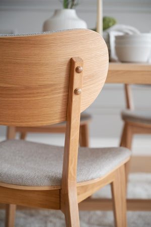 Närbild på stolsrygg i ljus ek med synliga träfibrer och grå stoppad sits vid matbord