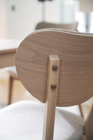 Närbild på stolsrygg i ljust trä med synlig ådring och grå stoppning, fäst med träslå och träplugg