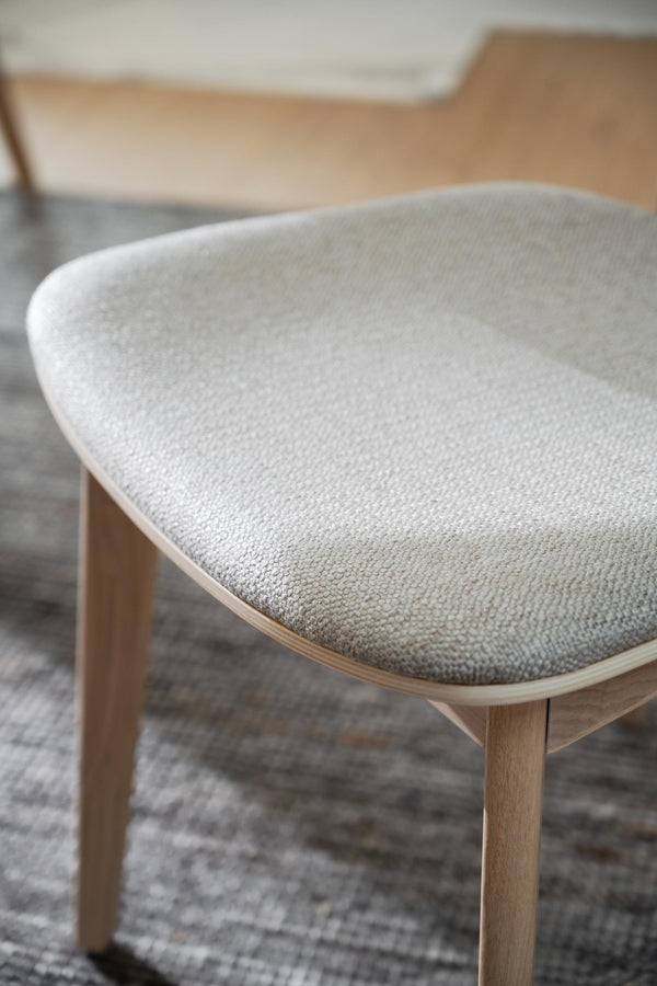 Stol med grå klädd sits och ljust trä, närbild på det kurvade sätet med textilklädsel