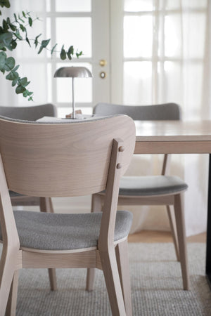 Ljusa trässtolar med grå stoppad sits runt matbord i modern skandinavisk matsal