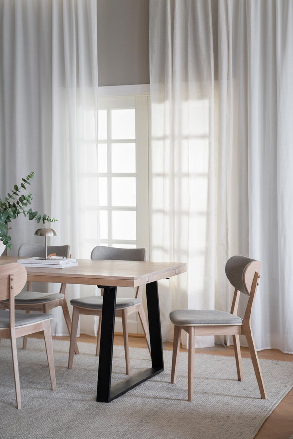 Matbord i ljust trä med svarta ben och grå stoppade stolar i ljust Skandinavisk matplats med vita gardiner