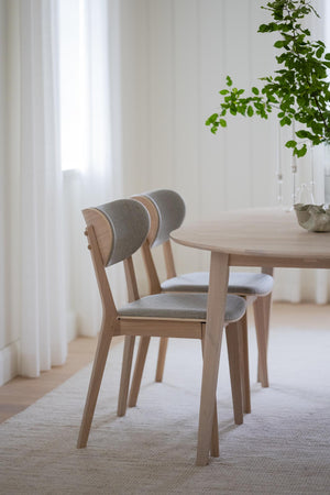 Ljusa trästolar med grå stoppad sits och rygg vid runt matbord i modern skandinavisk matsal