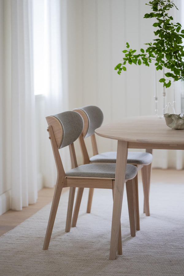 Ljusa trästolar med grå stoppad sits och rygg vid runt matbord i modern skandinavisk matsal