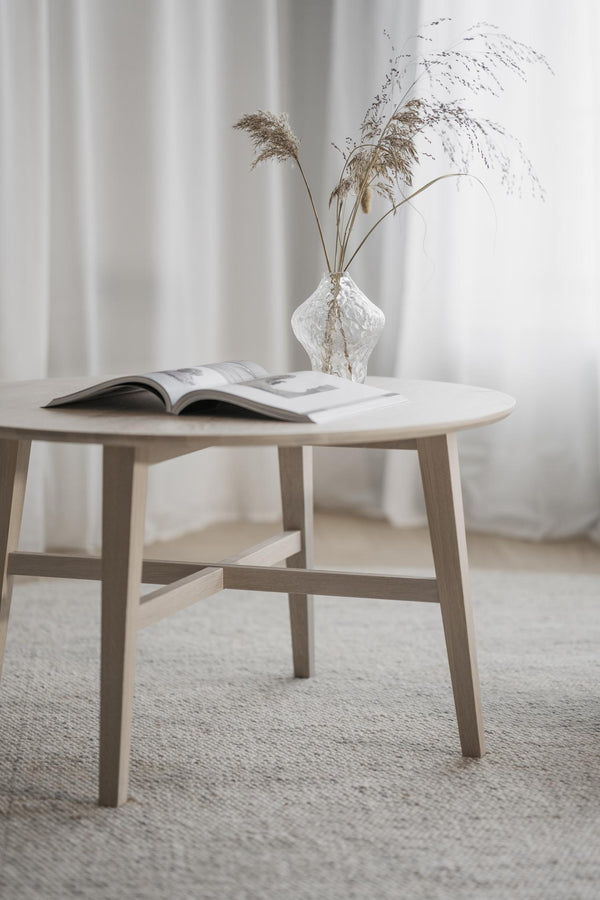 Runt soffbord i ljust trä med öppen bok och glasvas med torkade gräs i minimalistisk inredning