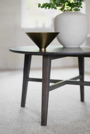 Soffbord i mörkt trä med konisk metallskål i mässing och vit vas med grön växt