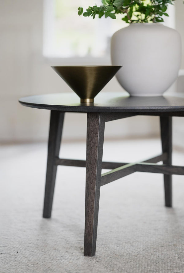 Soffbord i mörkt trä med konisk metallskål i mässing och vit vas med grön växt