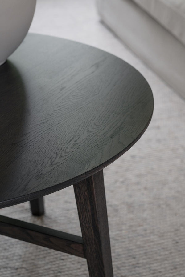 Soffbord med rund bordsskiva i mörkbetsad ek och träben, fotograferat från sidan