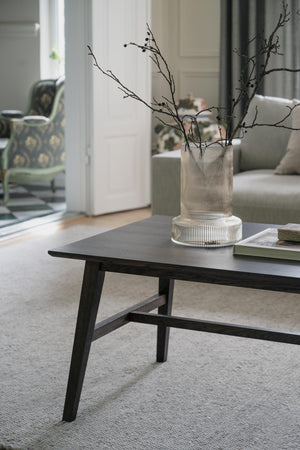Svart soffbord i trä med glasvas och grenar som dekoration i modernt vardagsrum