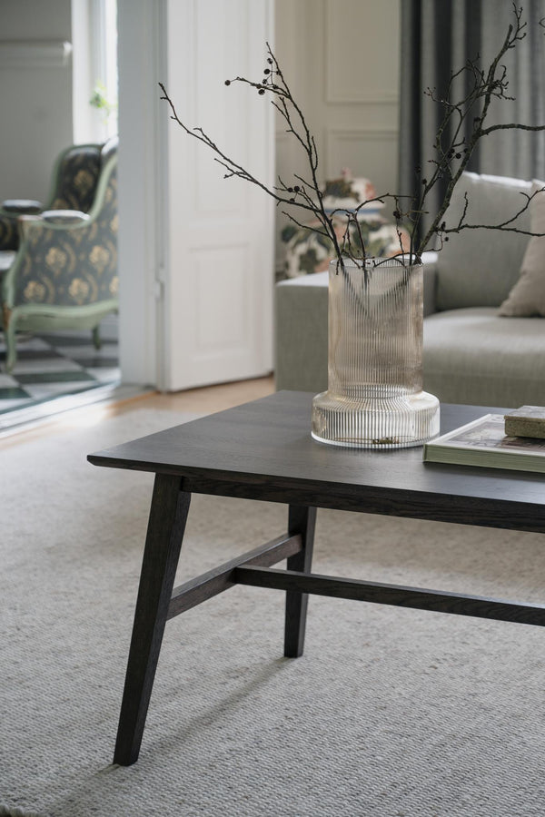 Svart soffbord i trä med glasvas och grenar som dekoration i modernt vardagsrum