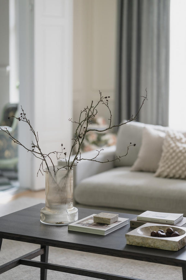 Glasvas med dekorativa kvistar på soffbord i modernt vardagsrum med böcker och dekoration