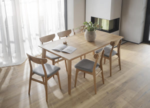 Matbord i ljust trä med sex stolar och grå dynor i ljus Skandinavisk matsal med öppen spis