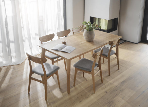 Matbord i ljust trä med sex stolar och grå dynor i ljus Skandinavisk matsal med öppen spis