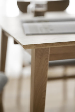 Närbild på bordskant i ljust trä med synlig årsring och ben i massiv ek