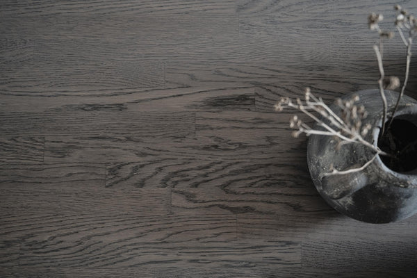 Mörk ekparkett med synlig trästruktur och dekorativ skål med torkade växter