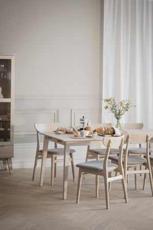 Ljus matgrupp i trä med sex stolar och grå dynor, dukad med frukost i skandinavisk matsal