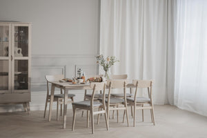 Ljus matgrupp i trä med sex stolar och skåp i skandinavisk matsal med vita väggar och gardiner