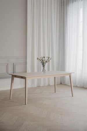 Ljust träbord i ek med smal design och vas med torkade blommor i minimalistiskt rum med vita gardiner