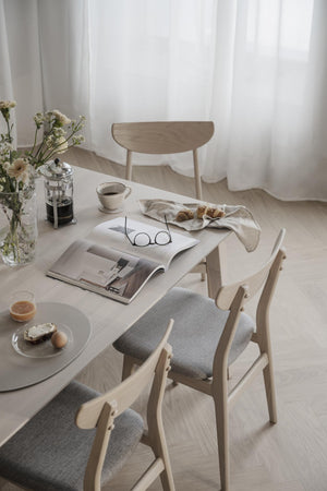 Ljus matplats med träbord, stolar med grå dynor, kaffebryggare, tidning och frukost i skandinavisk stil