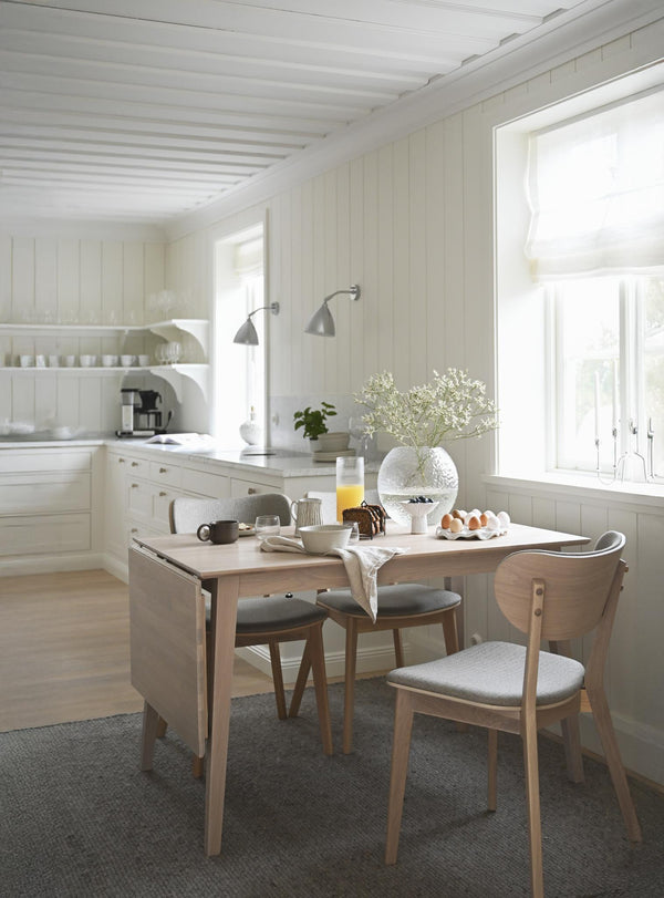 Ljust kök i skandinavisk stil med matbord i trä, vita skåp och vägglampor