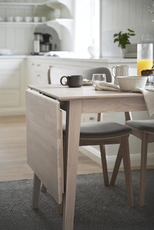 Matbord i ljust trä med frukostdukning, kaffemugg och juice i ljust kök med moderna stolar