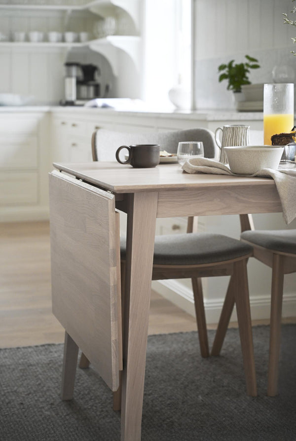 Matbord i ljust trä med frukostdukning, kaffemugg och juice i ljust kök med moderna stolar