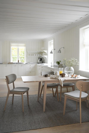 Ljust skandinaviskt kök med matbord i trä, grå stolar och vita skåpsluckor