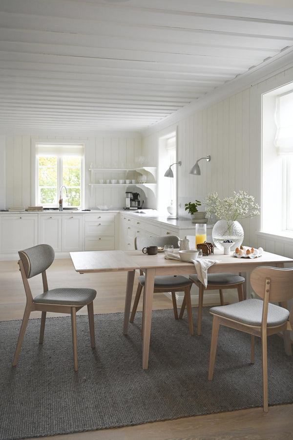 Ljust skandinaviskt kök med matbord i trä, grå stolar och vita skåpsluckor