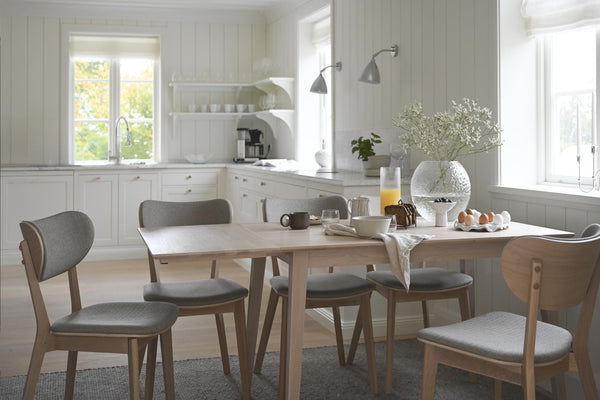 Ljust kök med matbord i trä och grå stoppade stolar, vita skåp och skandinavisk inredning