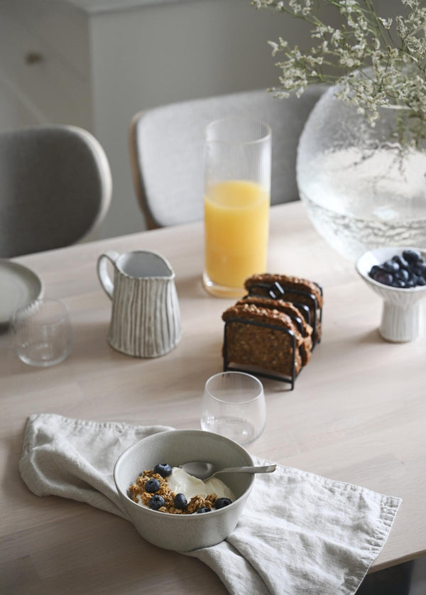 Frukostbord med granola i skål, blåbär, juice, bröd och vita porslinskärl i minimalistisk stil