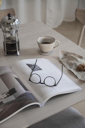 Glasögon på öppen bok med kaffekopp och french press på vitt bord - mysig läshörna