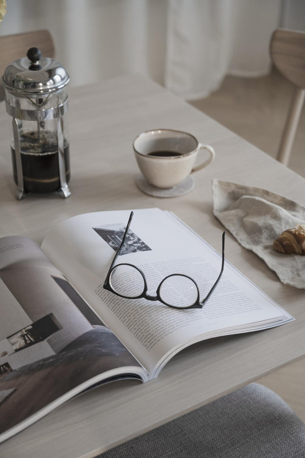 Glasögon på öppen bok med kaffekopp och french press på vitt bord - mysig läshörna