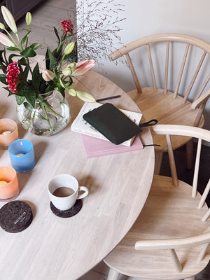 Rund matbord i ljust trä med stolar, kaffekopp, vas med blommor och färgglada ljuslyktor i skandinavisk inredning