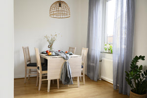 Ljust matrum med ljust trämöblemang, rotting taklampa, gråa gardiner och gröna växter