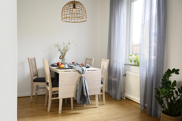 Ljust matrum med ljust trämöblemang, rotting taklampa, gråa gardiner och gröna växter