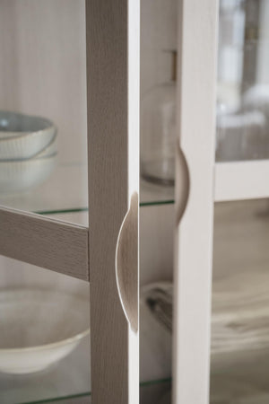 Närbild på vitrinskåp i ljust trä med glasdörr och hyllplan, elegant möbeldesign för vardagsrum