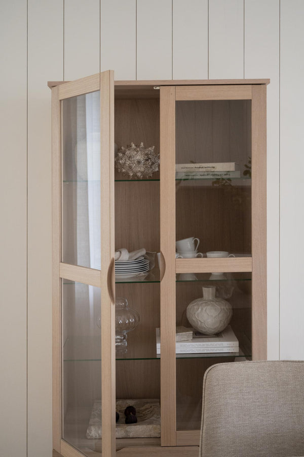 Vitrinskåp i ljust trä med glaspannor och tre hyllplan, inredd med porslin och dekorationsobjekt