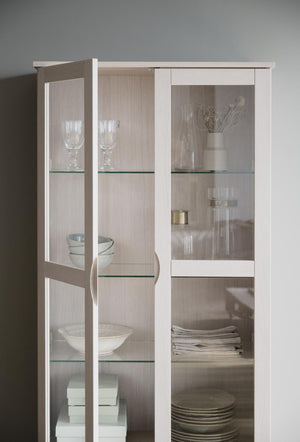 Vitrinskåp i vit med glashyllor och glasdörrar, inrett med glas, keramik och textilier